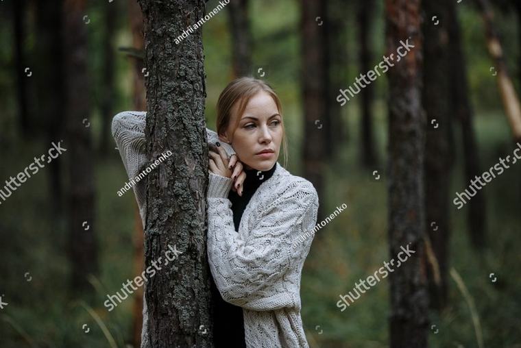A woman in a cream cardigan standing among pine trees