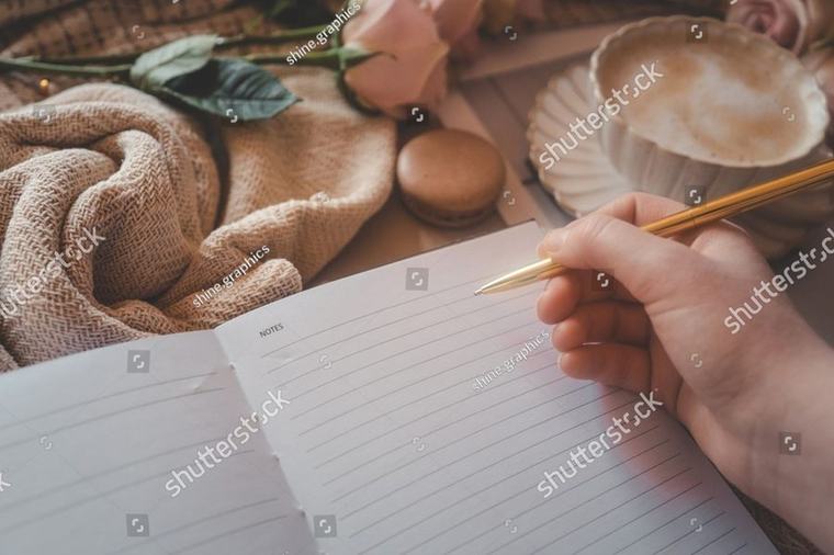 An open notebook, a gold pen and a cup of coffee on a knitted throw